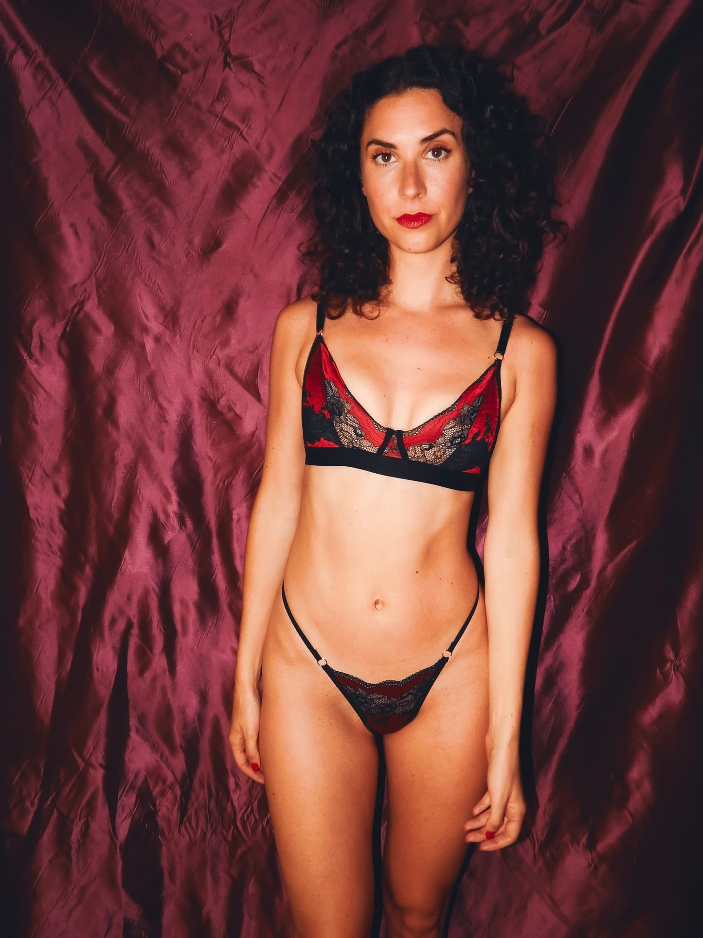 woman posing against red backdrop in black and red lace bralette