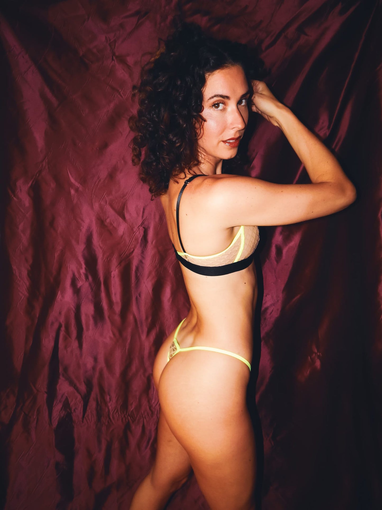 woman posing sideways in nude lingerie set with neon trim