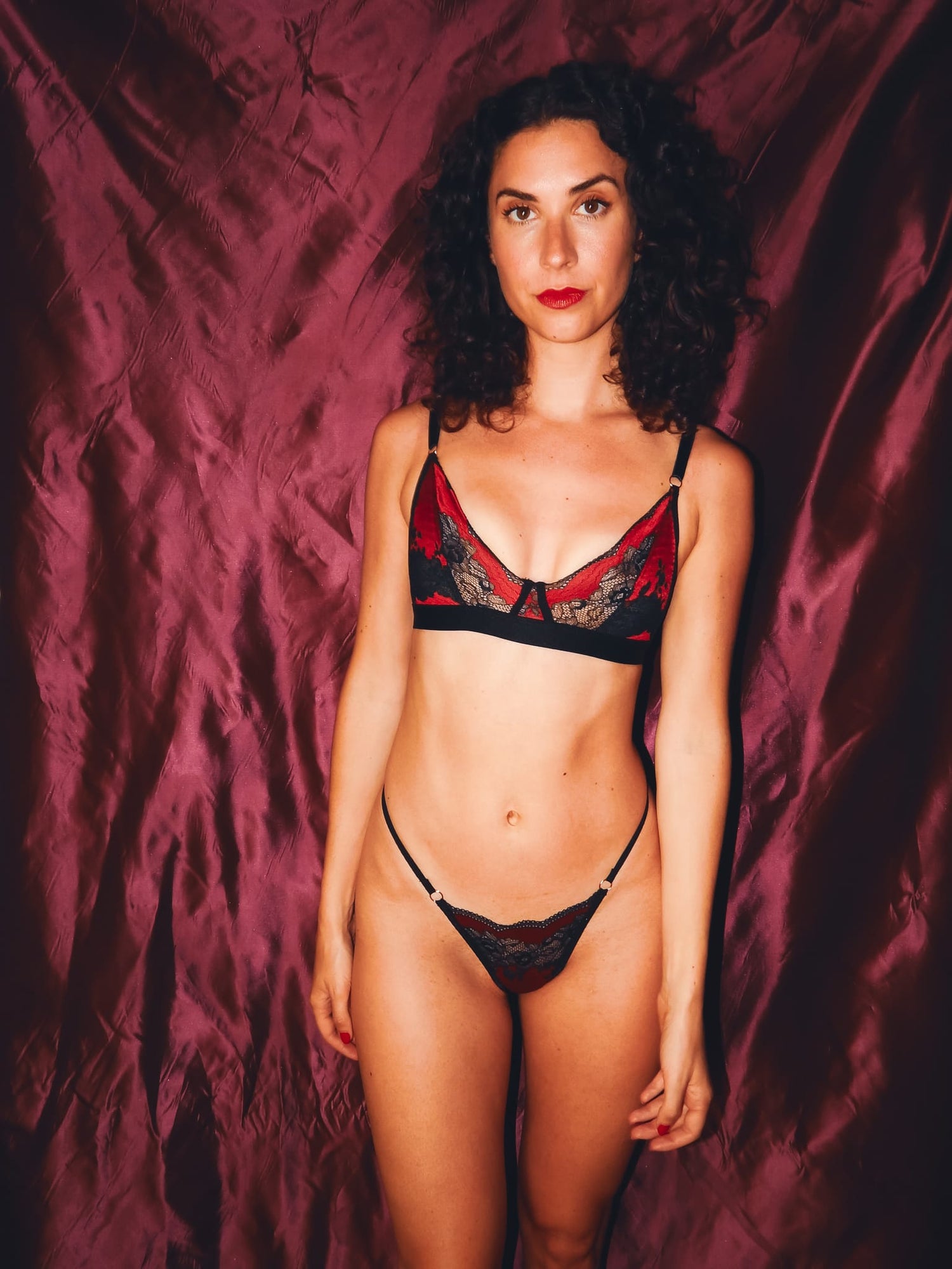 woman posing against red backdrop in black and red lace bralette