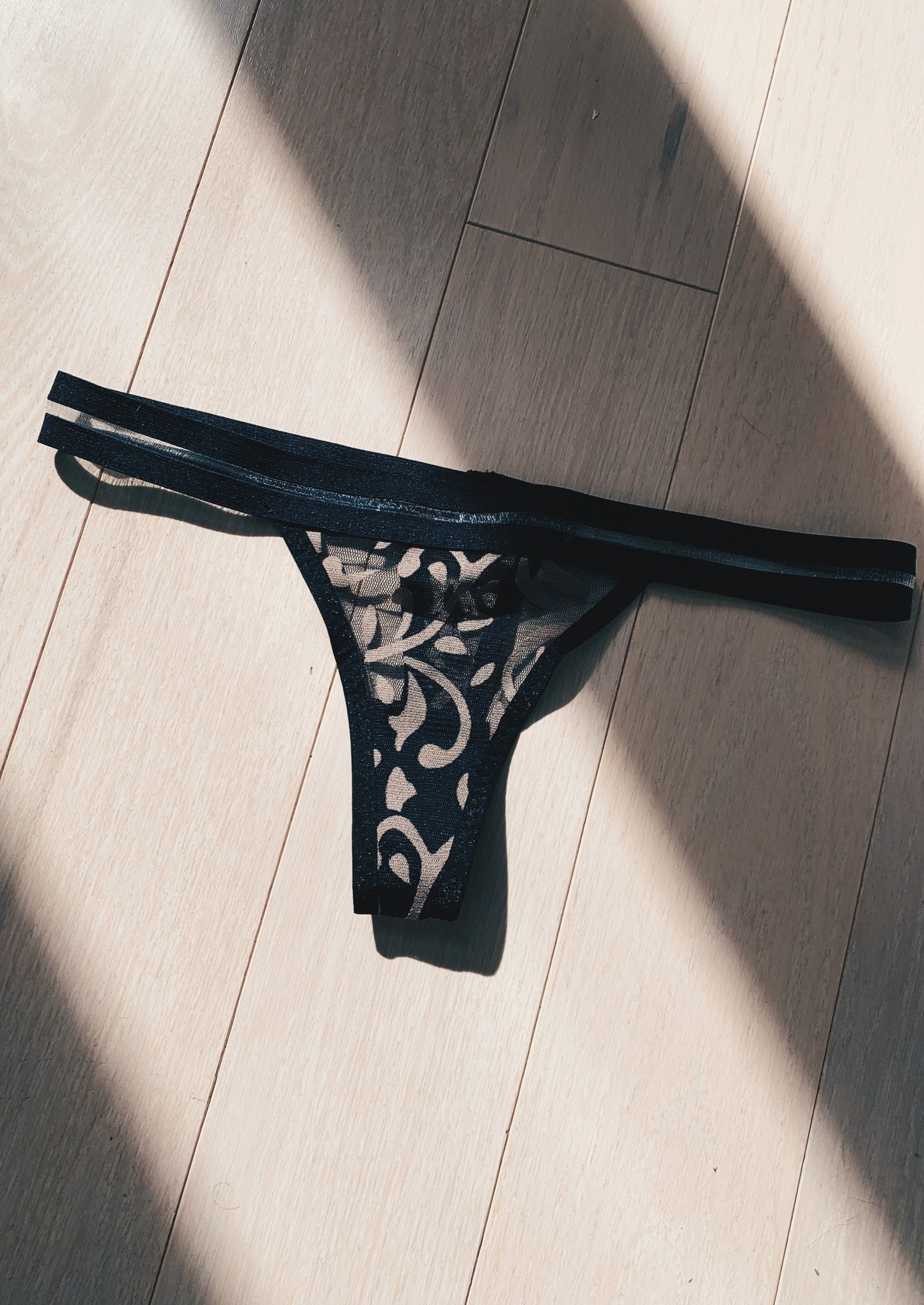 black semi see through thong with brown details against a wooden floor